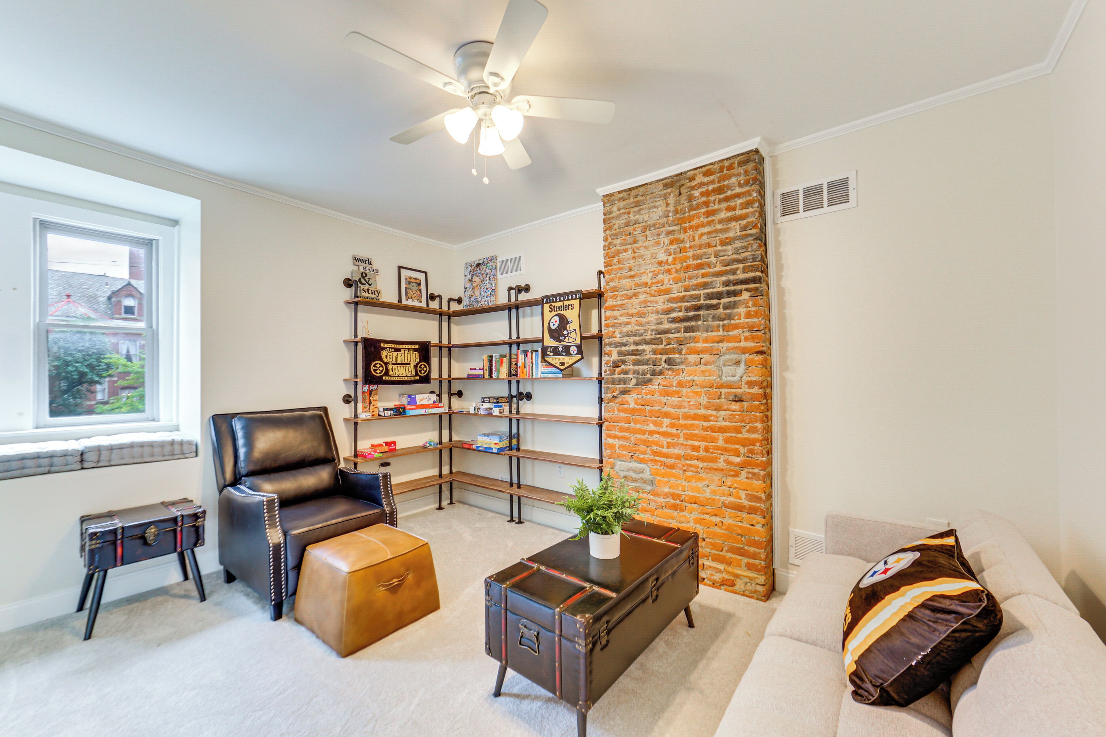 A living room with a leather chair, a sofa, a coffee table, a bookshelf, and a brick accent wall.