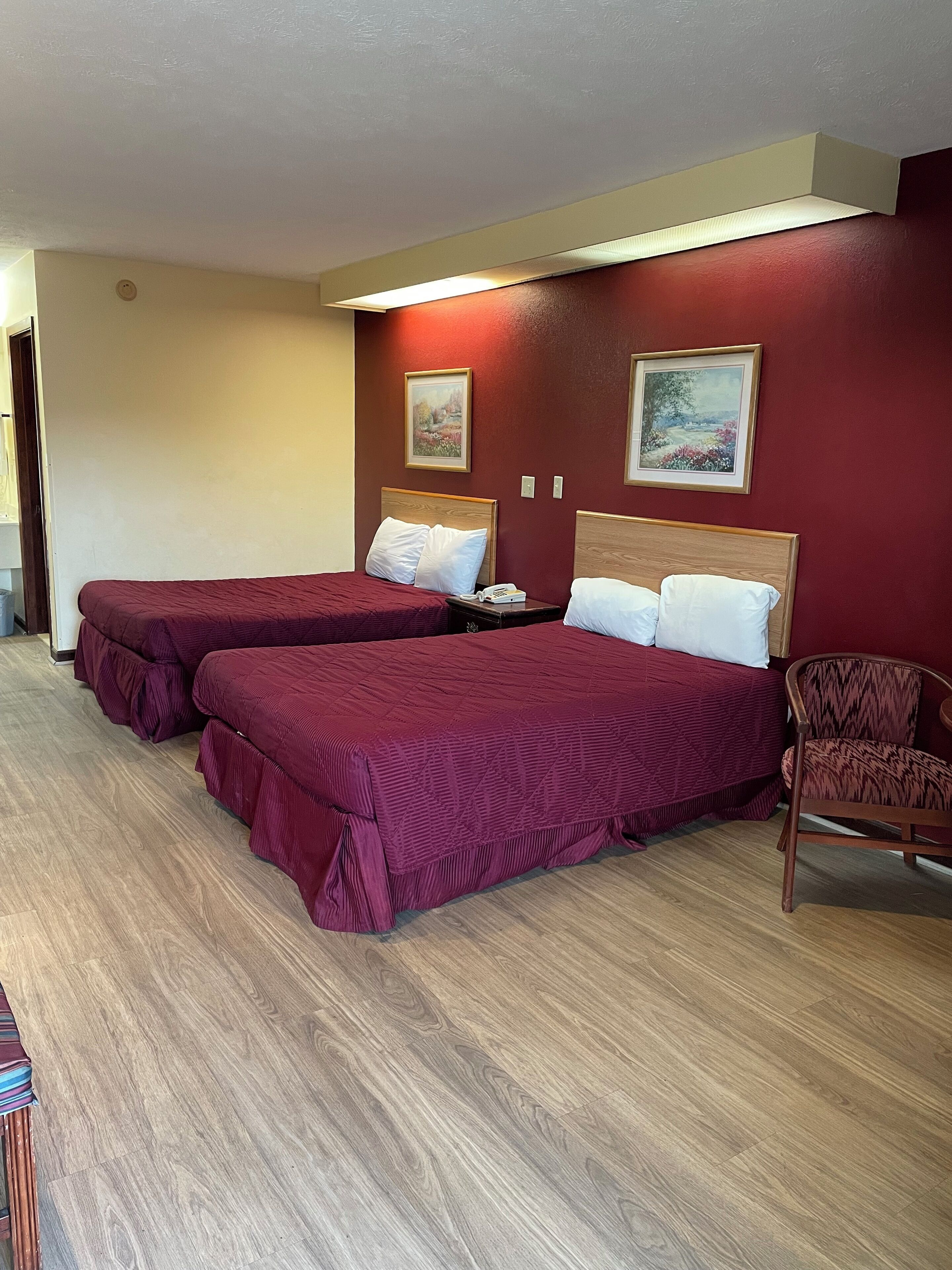 A hotel room with two beds, wooden flooring, and a chair.