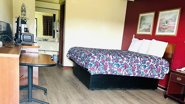 A hotel room with a bed, a desk, a chair, a TV, and a telephone. - Western Inn Express (Hazlehurst)