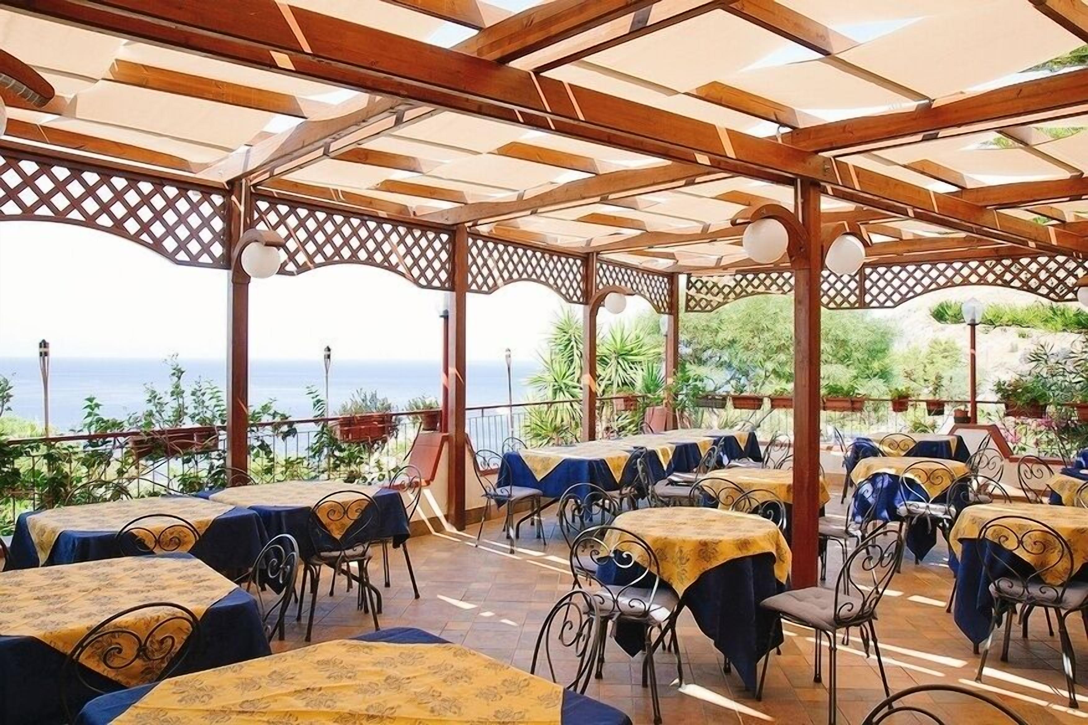 A covered outdoor dining area with tables and chairs, overlooking a scenic view.