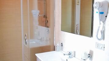 A modern bathroom with a glass shower enclosure, a white sink with a mirror above it, and a hairdryer mounted on the wall.