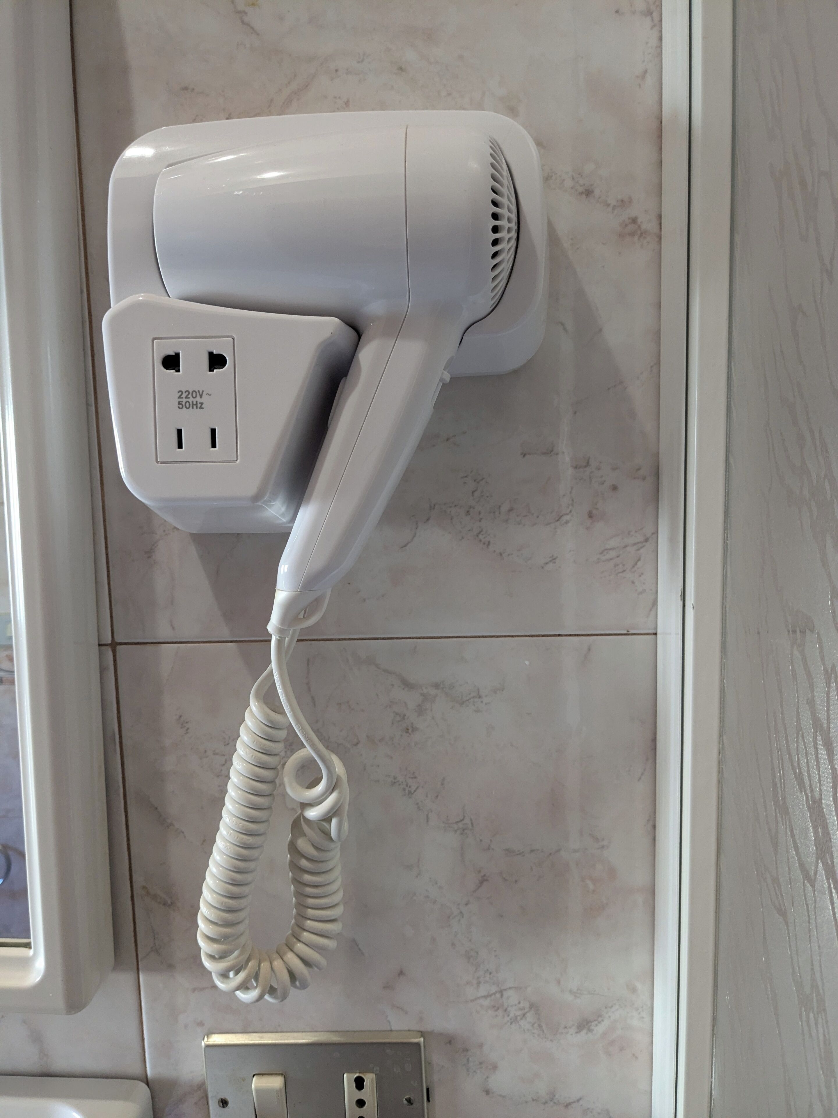 Un sèche-cheveux fixé au mur avec un cordon enroulé.