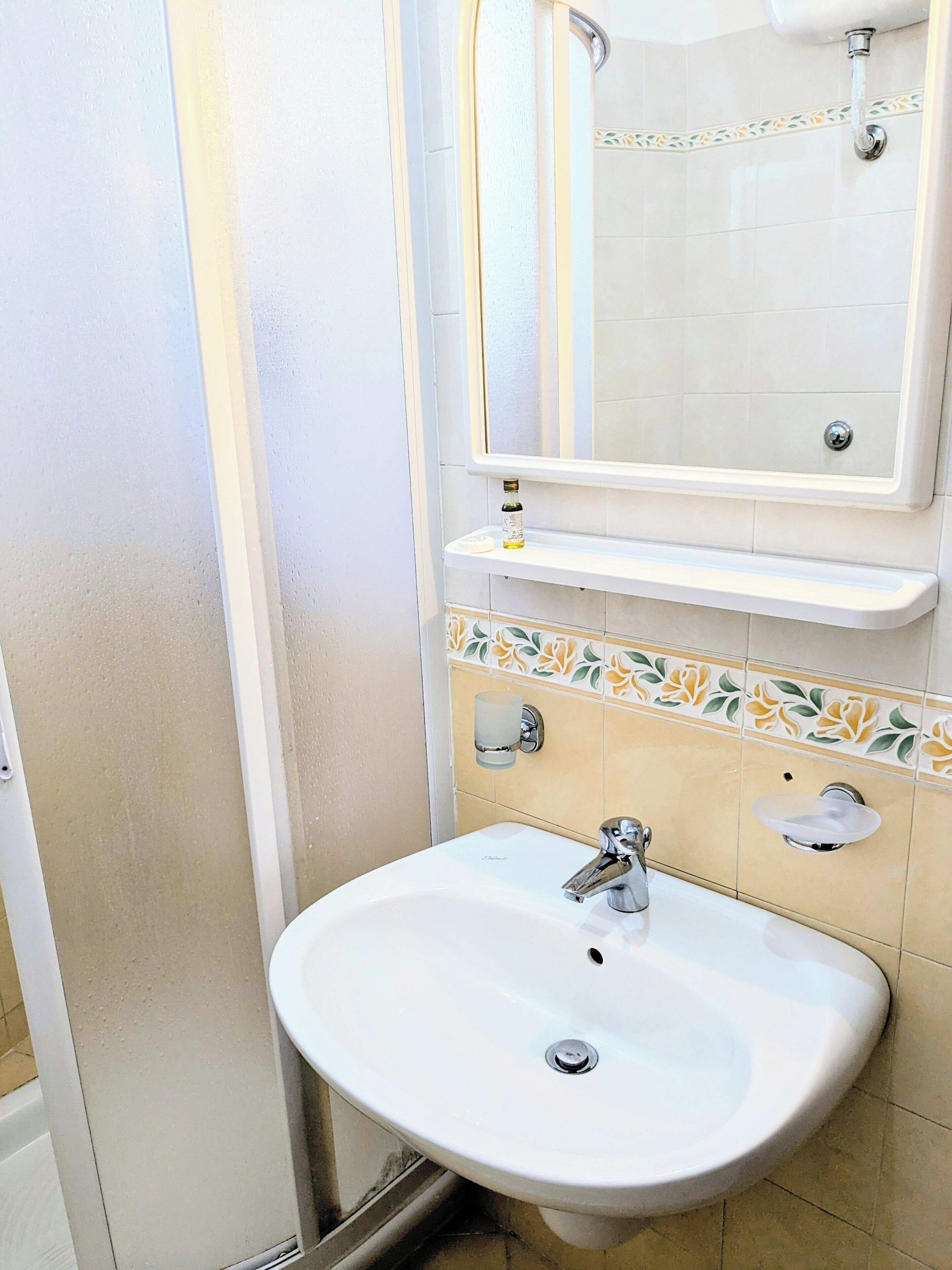 Un baño con un lavamanos blanco, un espejo encima y un estante pequeño con una botella.