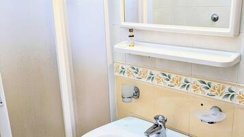 Un baño con un lavamanos blanco, un espejo encima y un estante pequeño con una botella.