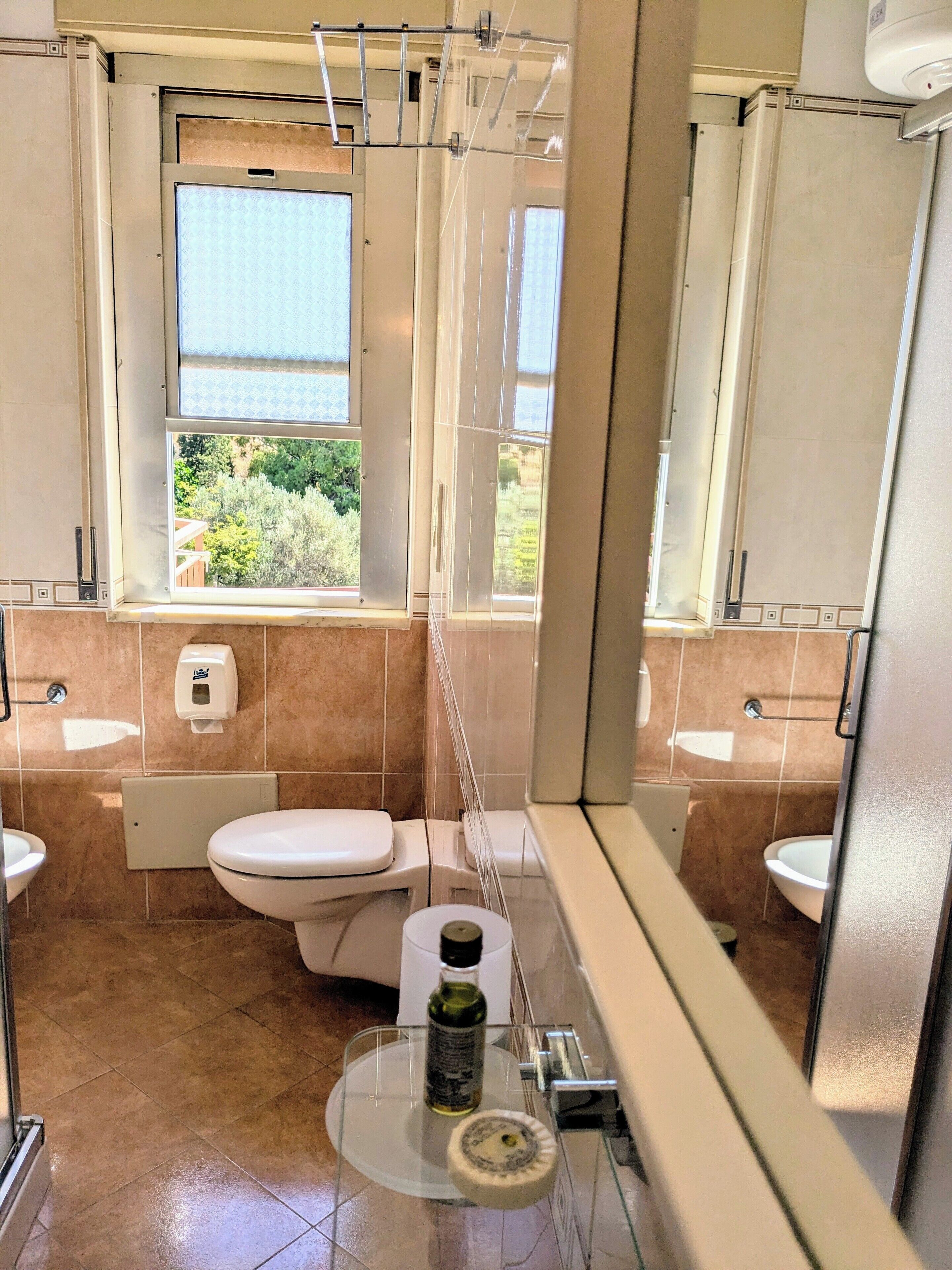 A bathroom with a toilet, bidet, and a window with a view of greenery.