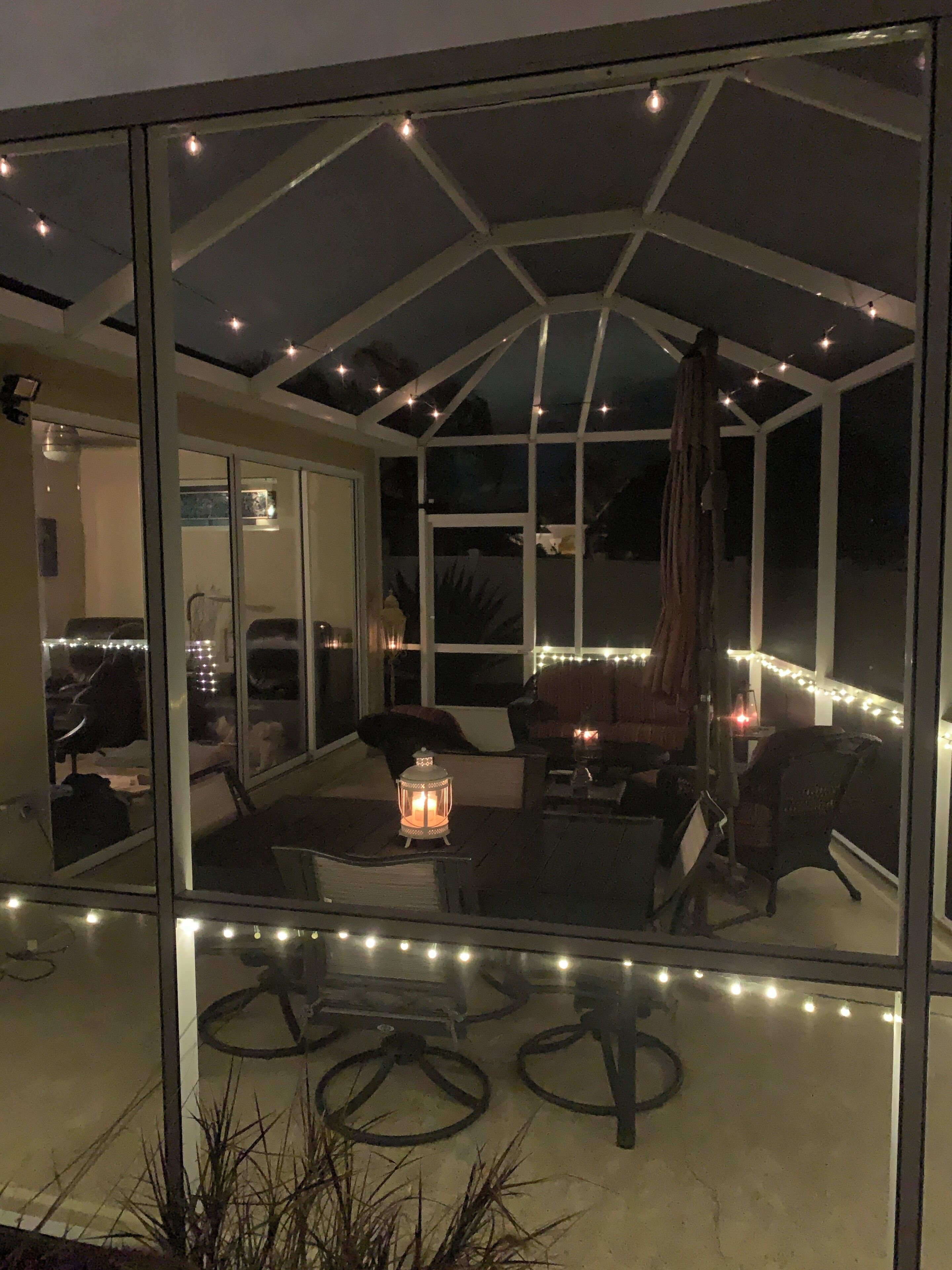 Un invernadero con techo de cristal, guirnaldas de luces y mobiliario que incluye una mesa y sillas.