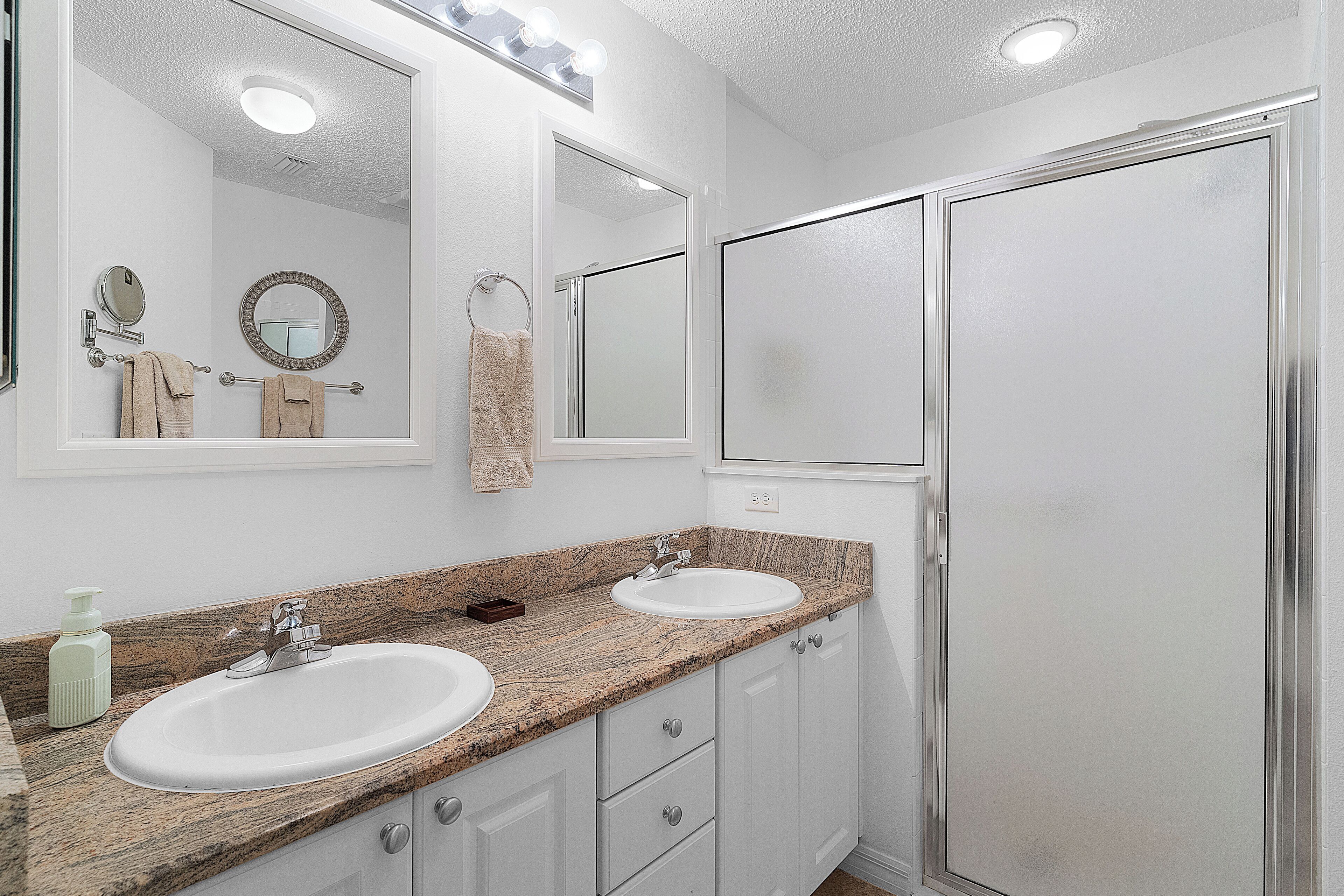 A bathroom with two sinks, a mirror, and a shower.