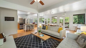 A spacious living area with a sofa, coffee table, and a ceiling fan. There is a kitchen area with a refrigerator and a dining table.