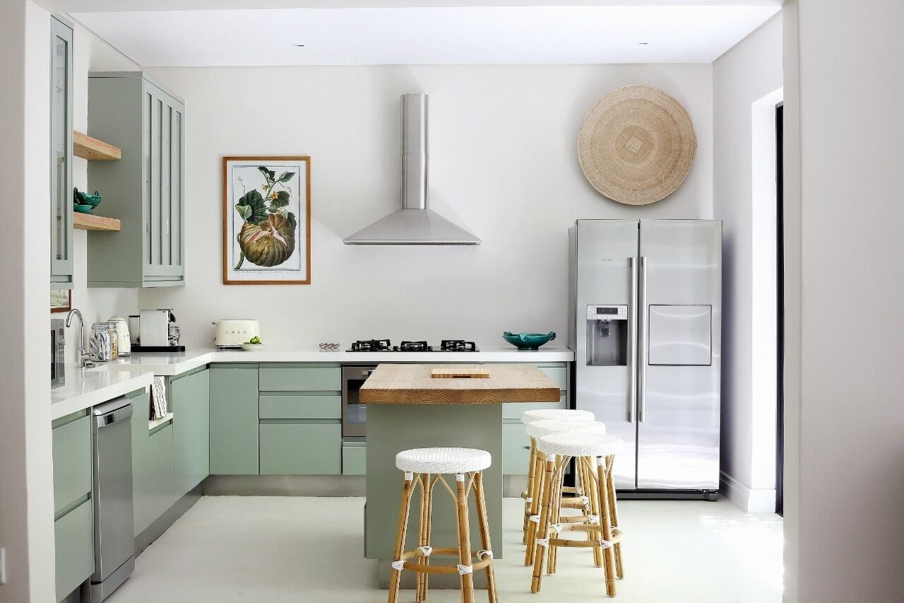 Une cuisine moderne avec des meubles de couleur verte, un îlot central doté de tabourets, un réfrigérateur en acier inoxydable et un panier suspendu.
