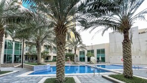Ein moderner Poolbereich im Freien mit Palmen, einem blauen Pool und einem Gebäude mit großen Fenstern im Hintergrund.