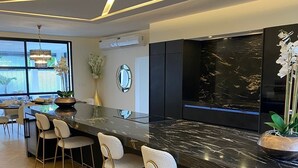 A modern kitchen with a marble countertop, bar stools, and a large window. - Empire Villa 2 Mon Plaisir (Paramaribo)