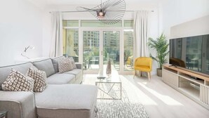 Ein modernes Wohnzimmer mit einem grauen Sofa, einem gelben Sessel, einem Glastisch und einem Fernseher auf einem Holzboden.