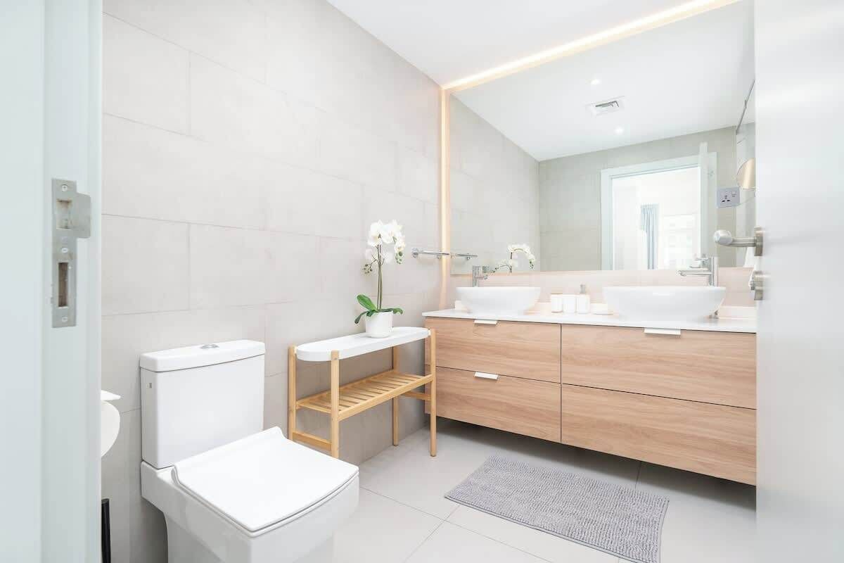 Une salle de bain moderne équipée de toilettes, d’un lavabo, d’un meuble-vasque et d’une petite étagère agrémentée d’une plante.
