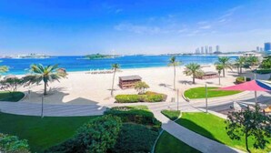 Ein Strand mit Palmen, einem klaren Himmel und einer entfernten Skyline einer Stadt.