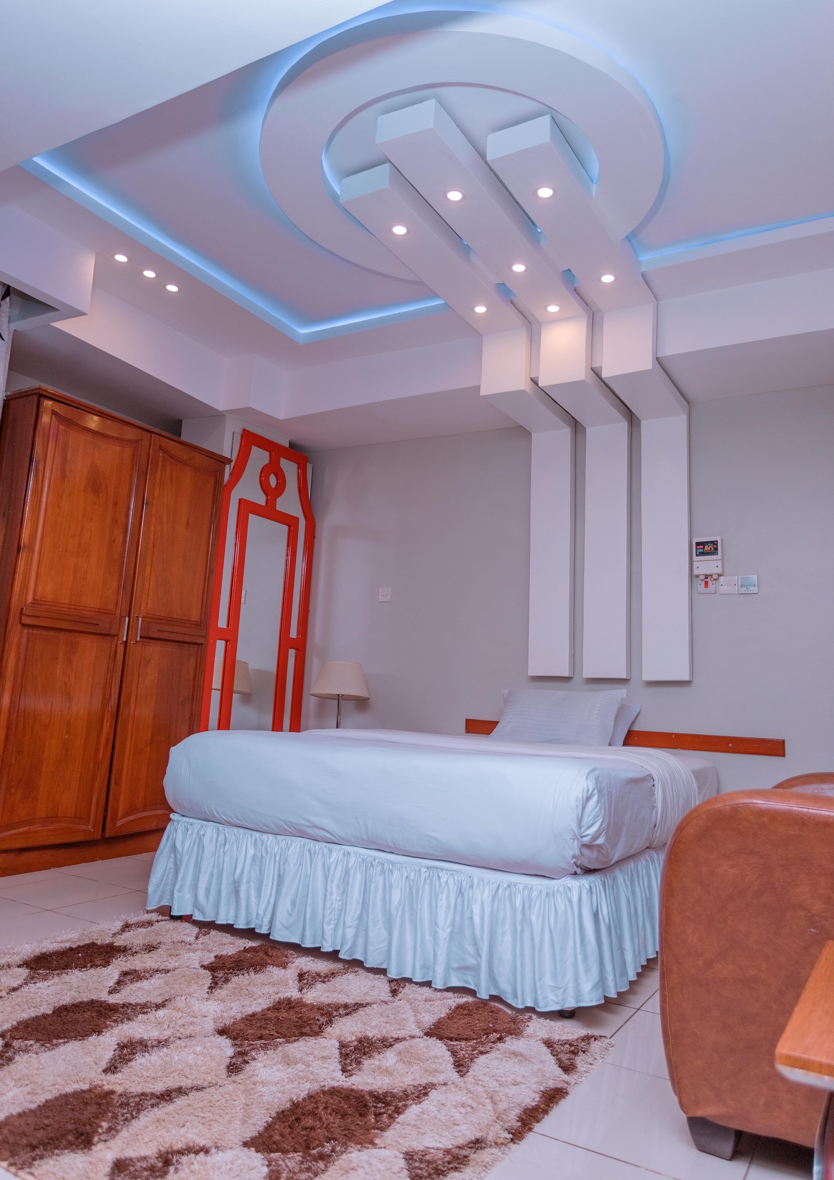 Una habitación de hotel moderna con una cama, un armario de madera, un espejo e iluminación empotrada en el techo.