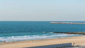 A beach with a rocky breakwater, clear skies, and a flag on the sand. - StayShort - Port De La Mer 1BR for 2, steps from the beach (Dubai)