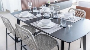 A dining table set with white plates, bowls, and wine glasses, surrounded by wicker chairs. - StayShort - Port De La Mer 1BR for 2, steps from the beach (Dubai)