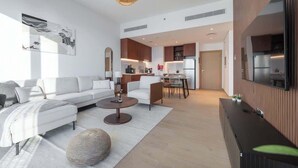 A modern living room with a sofa, coffee table, and ottoman, connected to a kitchen area with a dining table and chairs. - StayShort - Port De La Mer 1BR for 2, steps from the beach (Dubai)