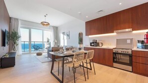 A modern kitchen with wooden cabinets, a gas stove, and a dining area with a table and chairs. - StayShort - Port De La Mer 1BR for 2, steps from the beach (Dubai)