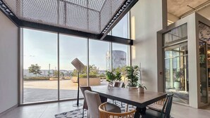 Et moderne spiseområde med et stort bord, stole og udsigt til byens skyline gennem store vinduer.