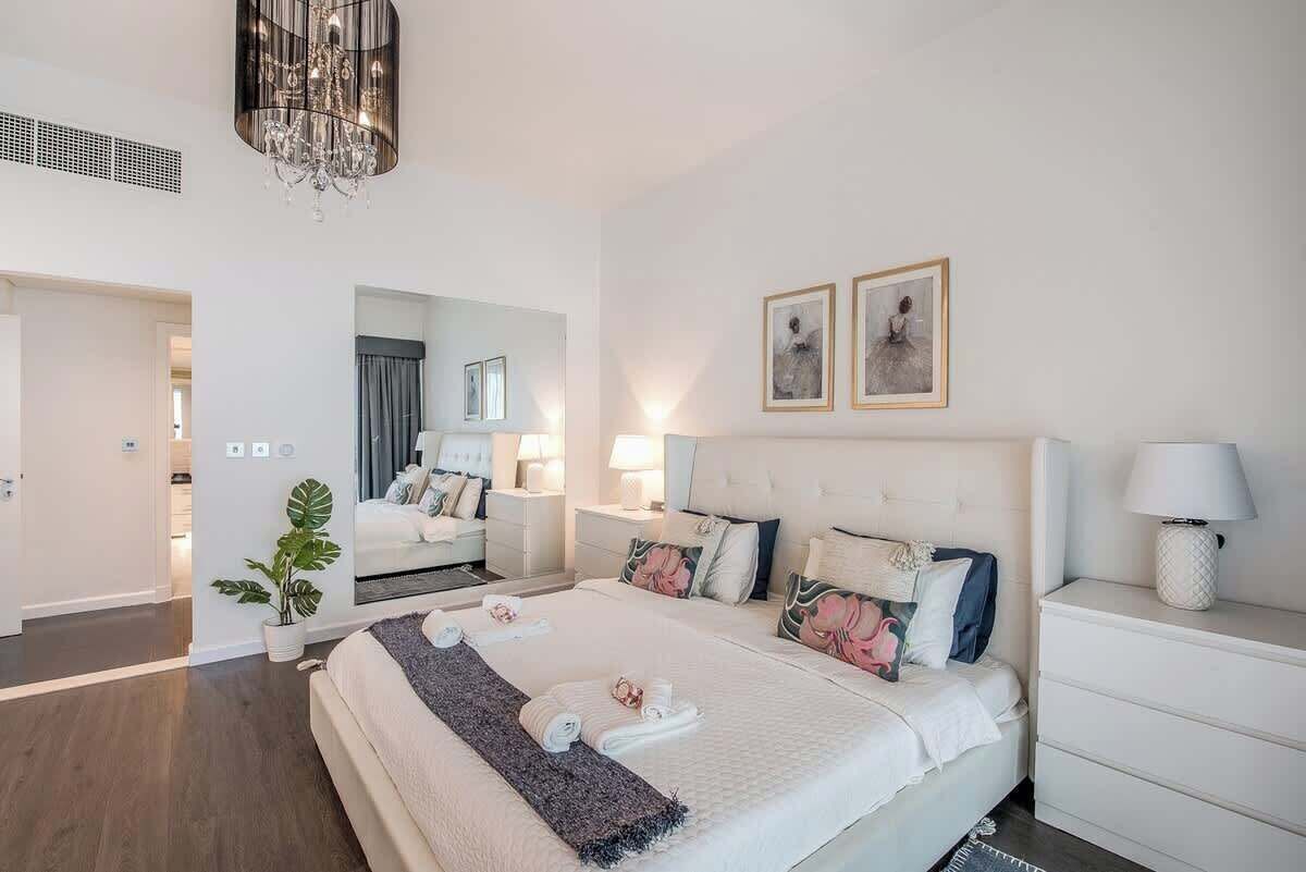A modern hotel room with a large bed, bedside tables, a chandelier, and artwork on the walls.