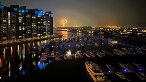 A marina with boats docked, a large building with illuminated windows, and a distant fireworks display. - StayShort - Superb 3BR in Palm Jumeirah With Unmatched Views! (Marina/JBR)
