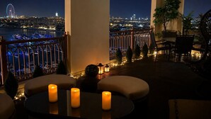A balcony with seating, candles, and a view of a cityscape at night. - StayShort - Superb 3BR in Palm Jumeirah With Unmatched Views! (Marina/JBR)