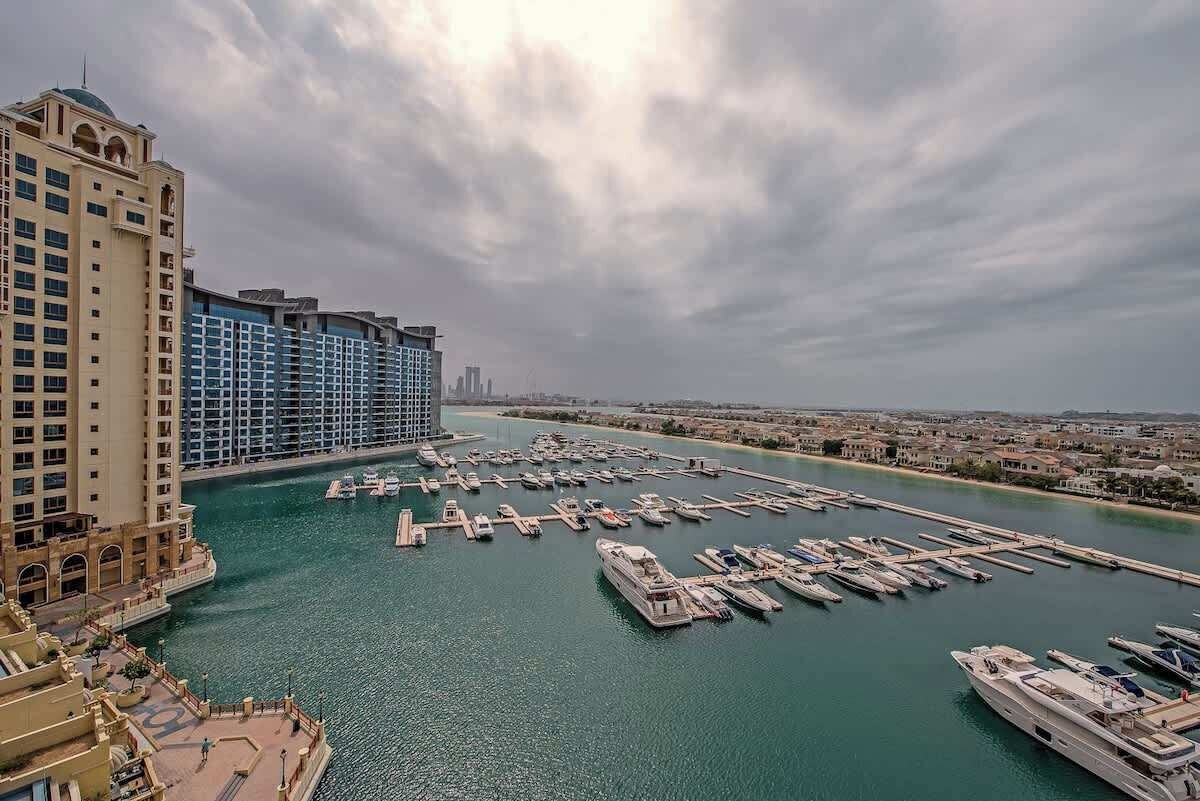 Een jachthaven met talloze boten afgemeerd, een groot hotel met meerdere verdiepingen, en een stadsgezicht op de achtergrond.