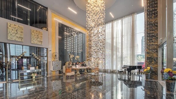 Un amplio hall con piso de mármol pulido, un piano de cola y una pared decorada con numerosos relojes.