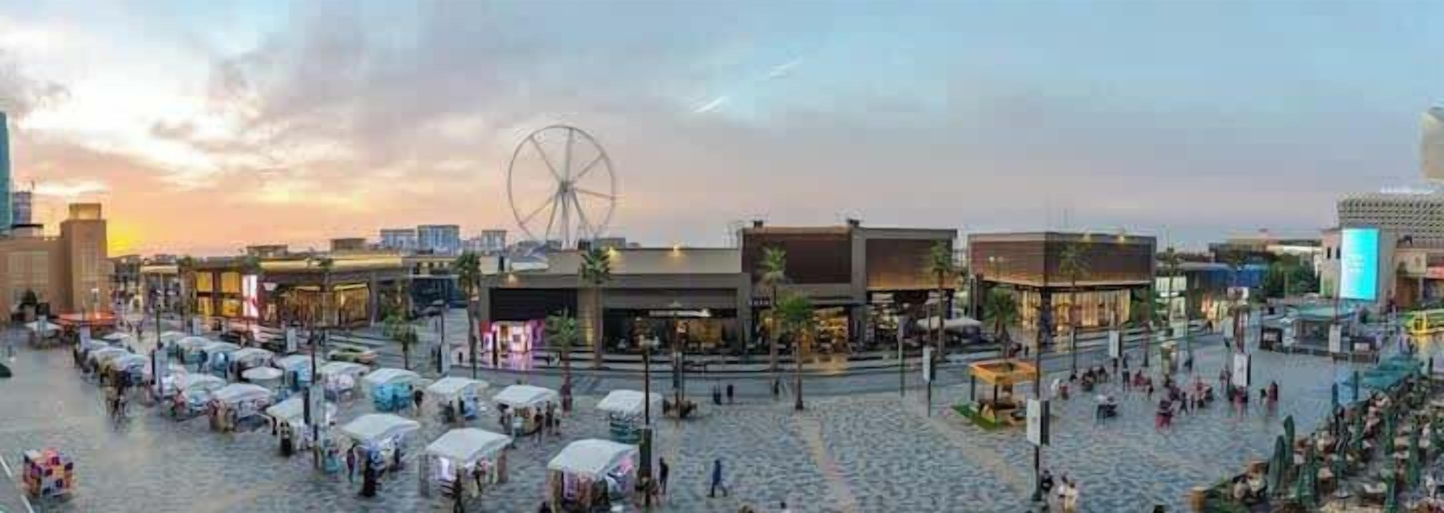 Una plaza con noria, tiendas y zonas de estar al aire libre.