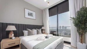 Una camera d'albergo moderna con un letto grande, due comodini con lampade, vista sulla città da una grande finestra e un quadro appeso al muro.