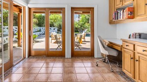 A kitchen with a sliding glass door leading to an outdoor patio, a white desk, and wooden cabinets.