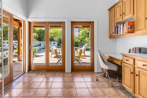 Une cuisine avec une porte-fenêtre coulissante donnant sur un patio extérieur, un bureau blanc et des armoires en bois.