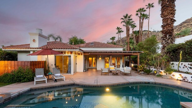 A house with a swimming pool, patio furniture, and a view of palm trees.