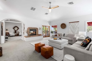 A spacious living room with a fireplace, a ceiling fan, and a view of the outdoors.