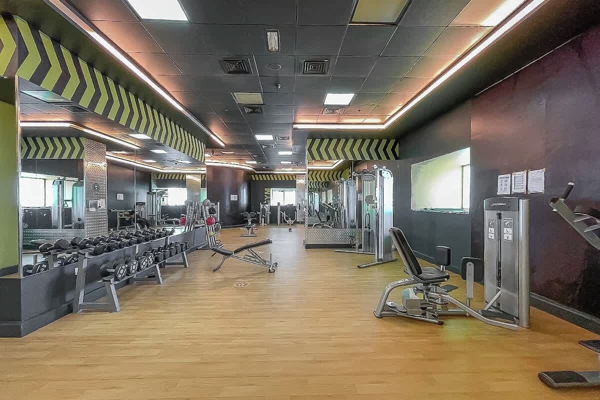 A gym with exercise equipment, mirrors, and a wooden floor.