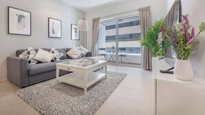 Een moderne woonkamer met een grijze bank, een witte salontafel en een groot raam met gordijnen.