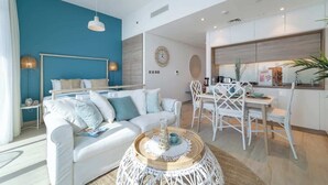 Una sala moderna con una pared azul de acento, un sofá blanco, un comedor con sillas blancas y una cocina con gabinetes blancos.