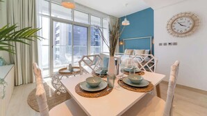 Un comedor moderno con una mesa dispuesta para cuatro personas, ventanas amplias y un reloj de pared decorativo.