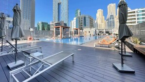 Un área de piscina en la azotea con sillones de descanso y sombrillas, rodeada de edificios altos.