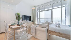 Una habitación de hotel moderna con una cama, una mesa de comedor con sillas, un televisor y ventanas amplias.