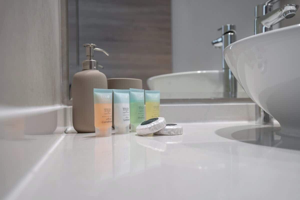 Une salle de bain avec un lavabo blanc, un flacon de lotion beige et trois récipients contenant des articles de toilette.