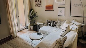 Een moderne woonkamer met een bank, een salontafel en een bijzettafeltje. Er hangen ingelijste kunstwerken aan de muur en staat een plant in de hoek.