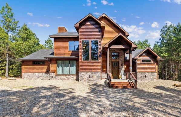 A log cabin with a stone foundation, a large front porch, and a chimney. - Pop's Place, Pet Friendly, Hot Tub, Play Set, Firewood, and More! (Broken Bow)