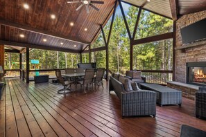 A covered outdoor patio with wooden flooring, wicker furniture, and a stone fireplace. - Pop's Place, Pet Friendly, Hot Tub, Play Set, Firewood, and More! (Broken Bow)