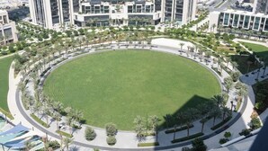 A circular park with a central lawn, surrounded by a road and palm trees. - StayShort - Captivating 1BR apartment in Dubai Creek Harbour! (Dubai)