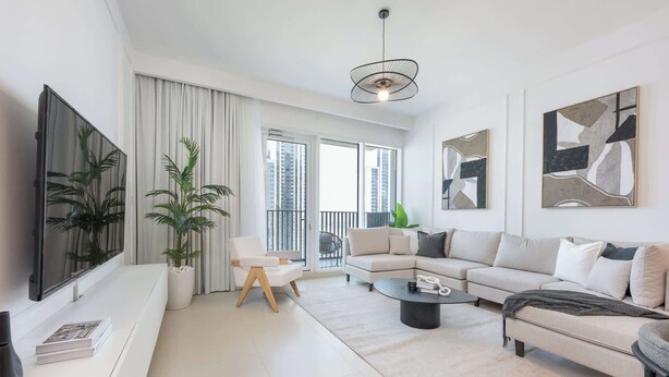 A modern living room with a sofa, coffee table, and a TV. There are plants, a balcony, and artwork on the walls. - StayShort - Captivating 1BR apartment in Dubai Creek Harbour! (Dubai)