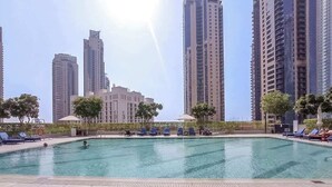 A swimming pool with lounge chairs and a view of tall buildings in the background. - StayShort - Captivating 1BR apartment in Dubai Creek Harbour! (Dubai)