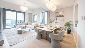 A modern living room with a dining area, large windows, and a chandelier.