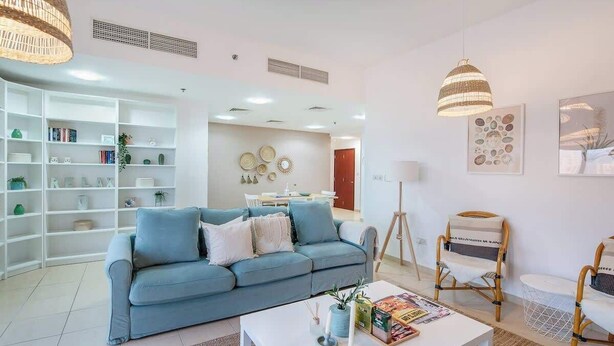 A modern living room with a blue sofa, white coffee table, and wicker chairs. - StayShort - Modern 2BR Retreat with Breathtaking Views in JBR (Dubai)